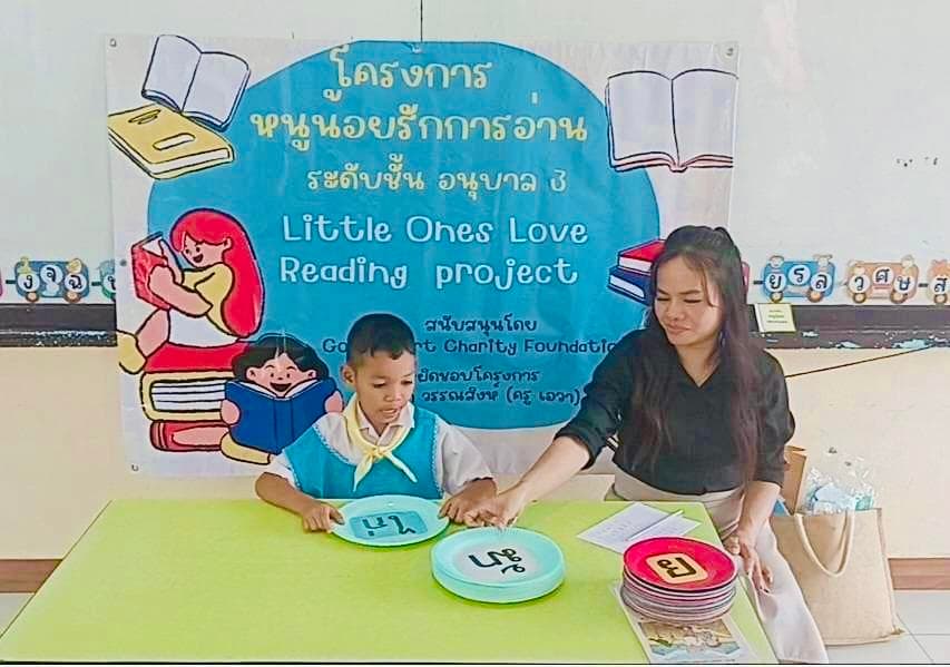 Ava working with a kindergarten pupil beneath the Little Ones Love Reading project banner